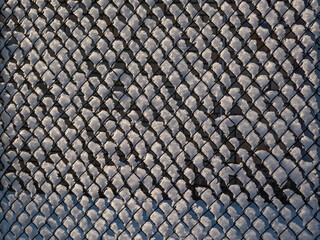 Metal fence covered with snow after snowfall in winter on bright sunny day. Geometrical patterns in...