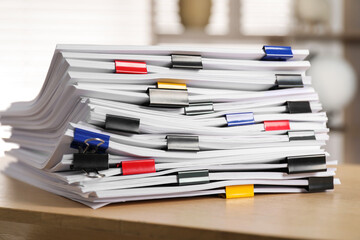 Colorful binder clips with sheets of paper on wooden table indoors, closeup