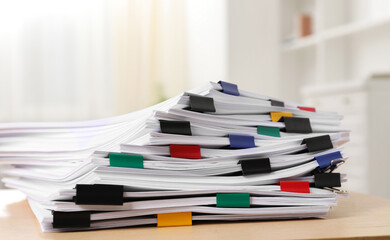 Colorful binder clips with sheets of paper on wooden table indoors, closeup