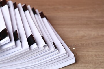 Binder clips with sheets of paper on wooden table, closeup. Space for text