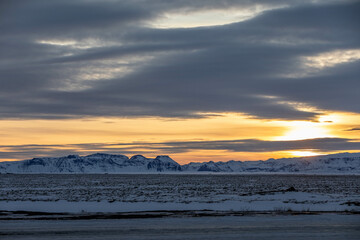 the sun sets behind snow covered mountains in Iceland