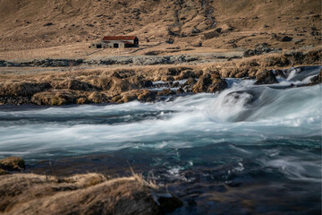 a small river in the south of Iceland with an old barn in the background