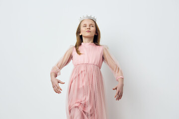 Young girl in a pink dress with a crown, exuding confidence and joy against a minimalist white...