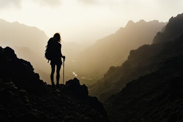 Fototapeta premium Dramatic Silhouette of a Hiker Standing on a Mountain Peak at Sunrise in Lomo Style