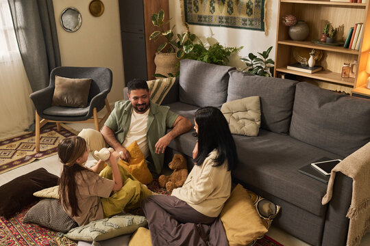 Family enjoying quality time together in cozy living room with carpeted floor and modern furniture, playing with plush toys and using electronic device, having fun and bonding