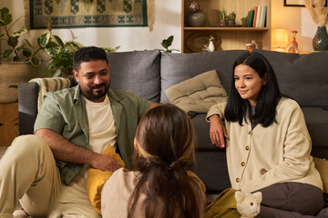 Portrait of family gathering in cozy living room. Parents engaging with child while sitting on...