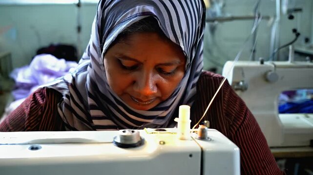  An Asian Indian woman, wearing a headscarf, working diligently as a seamstress in a textile factory. She is focused on sewing fabric using an industrial sewing machine.