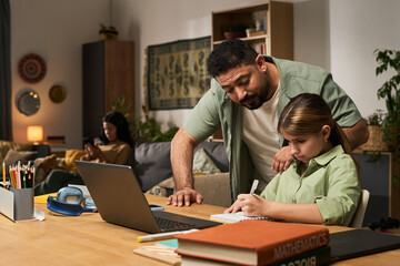 Supportive father helping daughter with homework in a cozy classroom setting. Shelves with books, school supplies, and decorations in background creating a structured yet warm atmosphere