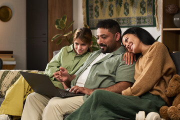 Family members sitting on couch in living room with laptop, smiling and enjoying each other's company in a warm and cozy setting