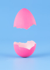 Single pink Easter Egg on blue background broken in pieces and opening like a hatching egg. Real dyed Easter egg shell cracked open vertically.