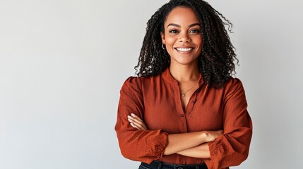 Confident woman with curly hair smiling, wearing a stylish blouse, standing with arms crossed against a neutral background.