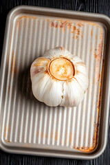 multiple roasted garlic bulbs at different stages of caramelization arranged on parchment paper with scattered herbs