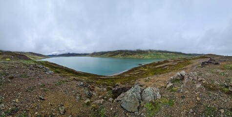 Panoramic view of turquoise lake and mountains partially covered by clouds in Iceland