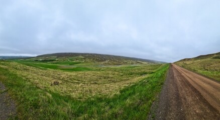 Fototapeta premium Panoramic view of gravel road crossing icelandic fields and hills