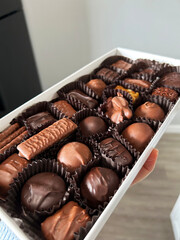 Assorted Chocolates Presented in a Decorative Box Held by a Hand in a Modern Kitchen Setting