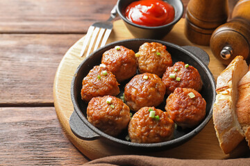 Tasty meatballs with green onion in baking dish served on wooden table