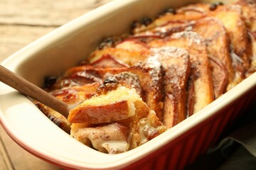 Taking tasty bread pudding from baking dish at wooden table, closeup