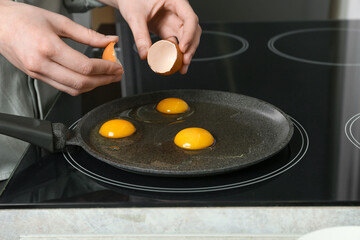 Woman breaking egg into frying pan in kitchen, closeup