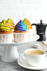 Delicious cupcakes with colorful cream and cup of coffee on grey textured table, closeup