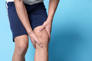 Young man suffering from pain in knee on light blue background, closeup. Space for text