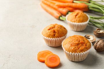 Tasty carrot muffins, fresh vegetables and walnuts on light grey table, closeup. Space for text