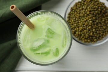 Fresh mung bean juice with ice in glass and seeds on white table, flat lay