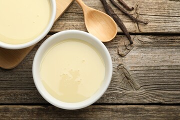 Tasty condensed milk, spoon and vanilla pods on wooden table, flat lay. Space for text