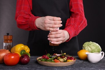 Woman salting tasty salad at dark textured table, closeup