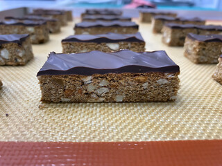 Nut bars topped with rich chocolate are neatly arranged on a cooling rack, showcasing the artistry of bakery creations in a cozy environment