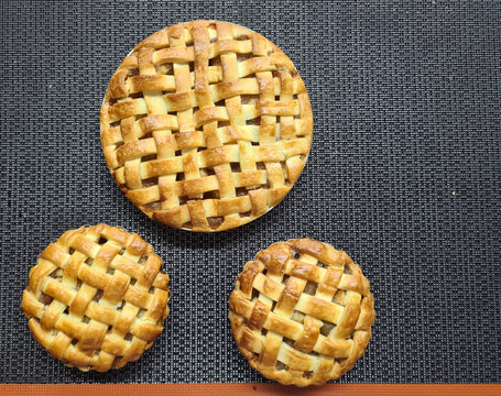 Three pie creations with a beautifully woven lattice crust, displayed on a dark textured background, highlight artisanal baking craftsmanship