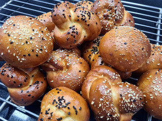 A variety of golden-brown bread rolls sprinkled with sesame seeds cool on a wire rack, filling the...