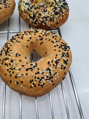 Bagels topped with white and black sesame seeds are cooling on a wire rack in a warm bakery setting