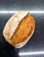 A rustic sourdough loaf rests on a kitchen counter after baking, showcasing its golden crust and...