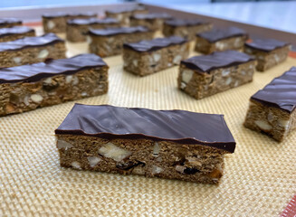 Nut bars topped with rich chocolate are neatly arranged on a cooling rack, showcasing the artistry of bakery creations in a cozy environment