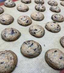 Rows of chocolate chip cookies cool on a baking sheet, ready for customers at a local bakery during busy morning hours