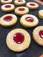 Round cookies filled with glossy red jelly and dusted with powdered sugar are arranged for sale at a local bakery, showcasing fresh treats