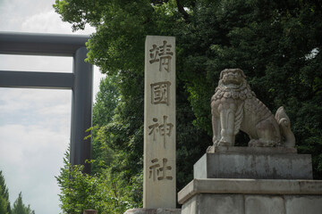 a lion-dog stone statue and a stone pillar with name of yasukuni shrine curved on it in front of the torii gate