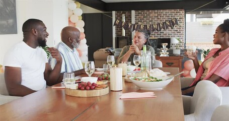 Happy black couple and senior parents at table and talking at retirement party in living room
