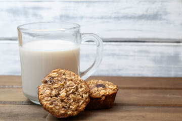 Glass of oat milk with mini oatmeal muffins on wooden background with copy space.
