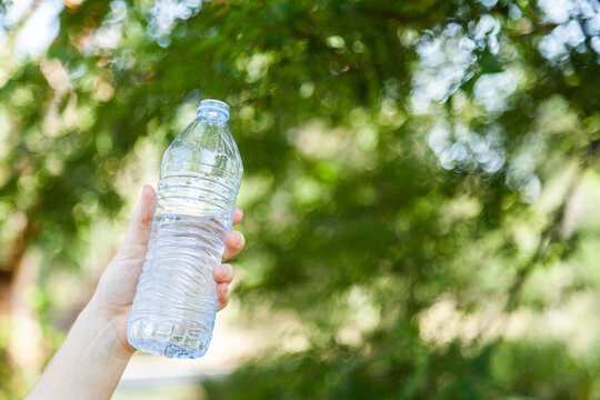 hand holding plastic water bottle outside with bokeh copy space