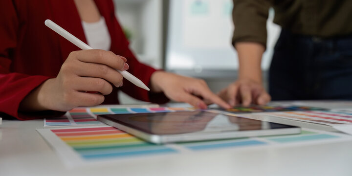 Digital Creation and Design Process. A close-up of a designer's hand using a stylus on a tablet alongside vibrant color charts.