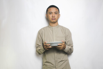 Muslim Man Bring White Plate with Badmood Gesture Wearing a Beige Islamic Shirt and Black Cap