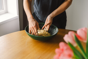 A woman in casual attire prepares dough for baking. She looks pleased and focused, enjoying the baking process in a light-filled kitchen.