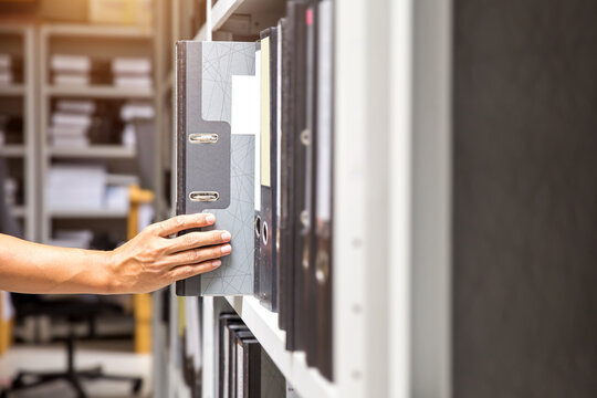 Hand of businessman office worker searching files and paperwork in the archive or document archiving storage room shelf for folder binder finding or data report record or workplace photo concept.