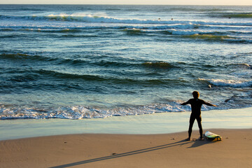 A male surfer in a wetsuit warms up with his surfboard beside him on the beach at Cabarita.