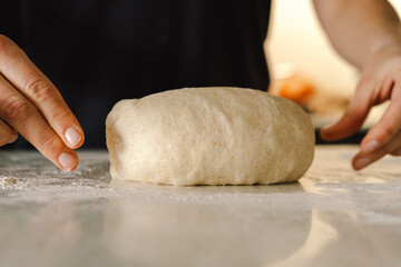 Hands are skillfully rolling and shaping dough on a clean kitchen countertop sprinkled with flour, healthy sourdough bread. The bright space suggests a cozy baking atmosphere.