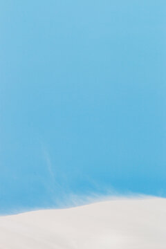 sand drifting on white dunes under blue sky vertical