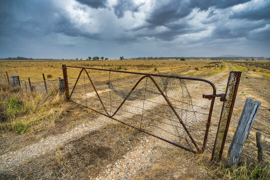Storm clouds over an old rusty gate on dry farmland