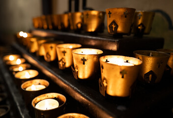 Votice candles flicker with golden light in a California Mission with prayer, cross, and worship in...