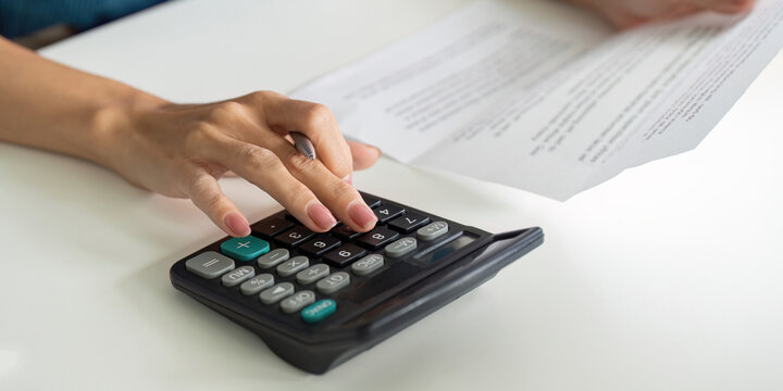 Financial Management and Saving Strategies. A person calculating expenses with a calculator while reviewing financial documents.